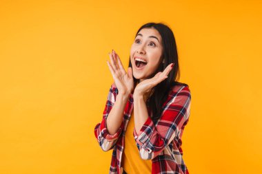 Şaşkınlığını ifade eden ve sarı arka planda izole bir şekilde yukarıya bakan hoş bir kadının fotoğrafı.