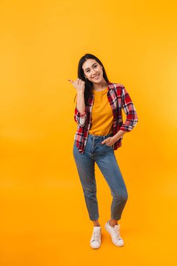 Neşe dolu genç bir kadının sarı arka planda parmakla işaret ettiği ve sırıttığı fotoğraf.