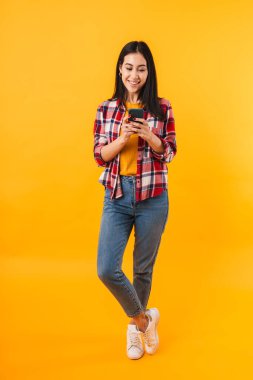 Sarı arka planda izole edilmiş cep telefonu kullanan neşeli esmer kadının fotoğrafı.