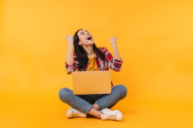 Sarı arka planda dizüstü bilgisayarı olan güzel bir kadının güzel bir jest yaptığı fotoğraf.