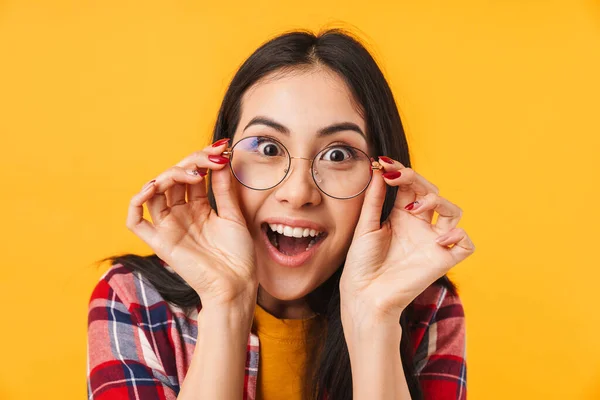 驚きのブルネットの女性を保持眼鏡とカメラを見ます絶縁上の黄色の背景 — ストック写真