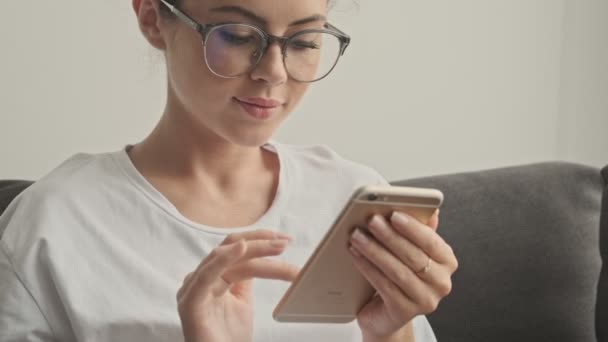 Gözlüklü Mutlu Esmer Kadın Evde Kanepede Otururken Akıllı Telefon Kullanıyor — Stok video