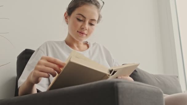 Evdeki Kanepede Otururken Gülümseyen Güzel Esmer Kadının Kitap Okumasını Izle — Stok video