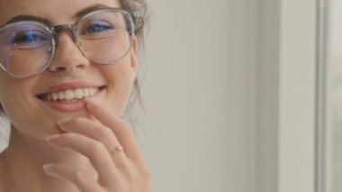 Gözlüklü güzel esmer kadının kameraya bakıp dudaklarına dokunuşunun yakın görüntüsü.