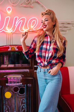 Eski Amerikan Kafesi 'nde müzik kutusuna yaslanırken güzel saç stili olan neşeli genç bir kadının fotoğrafı.