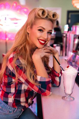 Güzel saç stili olan, milkshake içen ve Amerikan kahvesinde gülümseyen muhteşem, neşeli bir kadının fotoğrafı.