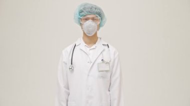 Genç Asyalı doktor, beyaz duvar arkasında steril üniformayla izole edilmiş. Vücut sıcaklığını temassız termometreyle ölçüyor.