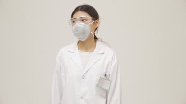 Genç Asyalı şaşkın, güvenilmez doktor kadın steril üniformalı beyaz duvar arkasında izole edilmiş.