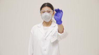 Genç Asyalı ciddi doktor kadın steril üniformalı beyaz duvar arkasında izole edilmiş.