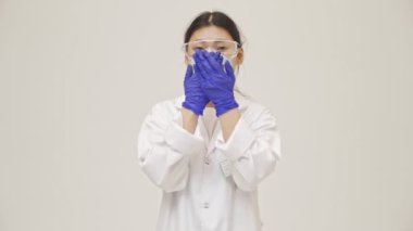 Genç Asyalı negatif doktor kadın, beyaz duvar arkaplanından ağzı kapalı, steril üniformayla izole edilmiş.