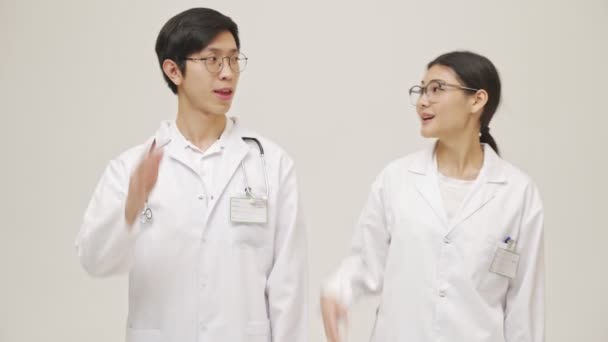 身穿无菌制服的积极乐观的年轻亚洲医生在白墙背景上摆出一副孤立无援的架势 相形见绌 — 图库视频影像