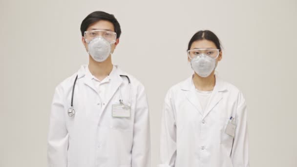 严肃的亚洲医生 身穿无菌制服 头戴口罩 站在白墙背景上 摆出一副孤立的样子 — 图库视频影像