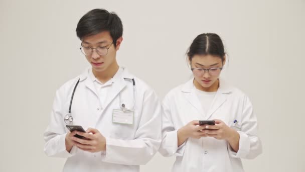 긍정적 아시아 의사들 핸드폰을 사용하는 제복을 고립된 채누워 것으로 나타났습니다 — 비디오