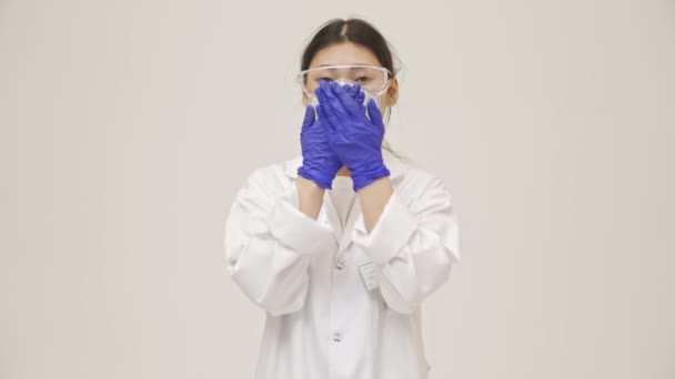 年轻的亚洲阴性女医生 身穿无菌制服捂着嘴 被隔离在白墙后面 — 图库视频影像
