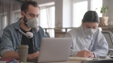 Genç konsantre iş adamları ofiste Coronavirus yüzünden maske takarak dizüstü bilgisayar kullanarak not tutuyorlar.