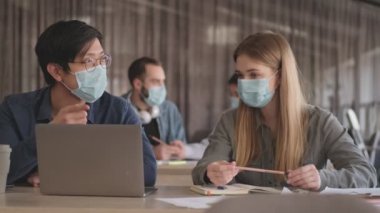 Genç konsantre iş adamları ofiste Coronavirus yüzünden maske takarak birbirleriyle konuşuyorlar.