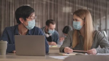 Genç konsantre iş adamları ofiste Coronavirus yüzünden maske takarak birbirleriyle konuşuyorlar.