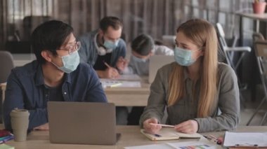 Genç pozitif iyimser iş adamları ofiste Coronavirüs yüzünden maske takarak birbirleriyle konuşuyorlar.