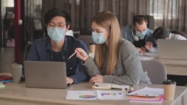 Genç konsantre iş adamları ofiste birbirleriyle konuşuyorlardı. Coronavirus yüzünden maske takıyorlardı. Laptop bilgisayar kullanıyorlardı.