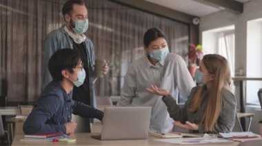 Genç pozitif iş adamları ofiste Coronavirus yüzünden maske takarak birbirleriyle konuşuyorlar.