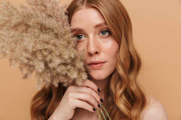 Portrait closeup of gorgeous young half-naked woman with long hair holding field flowers isolated over beige background