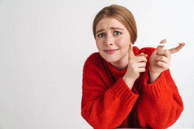 Kafası karışmış kırmızı kazaklı güzel bir kadının fotoğrafı. Kameraya bakıyor ve beyaz duvarın üzerinde izole bir kalem tutuyor.