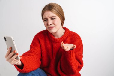 Kafası karışmış genç bir kadının beyaz duvar arkasında yalnız poz verip cep telefonuyla konuşması..