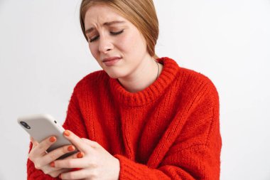 Hoşnutsuz genç bir kadının beyaz duvar arkasında cep telefonu kullanarak poz vermesi..