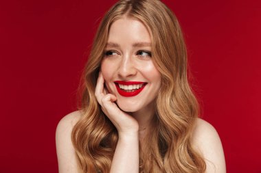Kırmızı duvar arkasında izole edilmiş, parlak kırmızı rujla poz veren güzel bir genç kadın resmi.