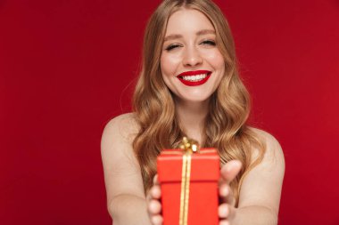 Kırmızı duvar arkasında izole edilmiş kırmızı rujlu, mutlu, genç bir kadın görüntüsü size Noel hediyesi veriyor..