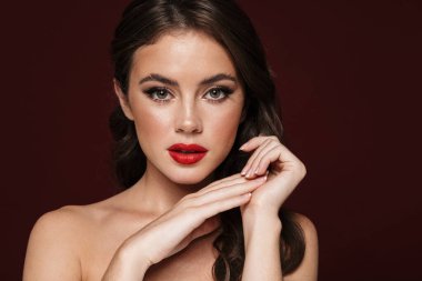 Güzel makyajlı çekici üstsüz bir kadın resmi. Burgonya arka planında izole edilmiş kameraya bakıyor.