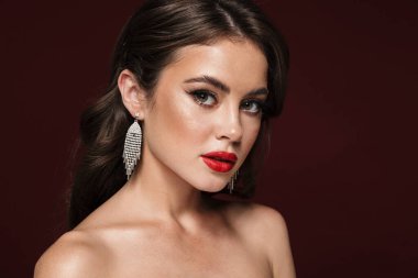 Küpe takan çekici, üstsüz bir kadın resmi. Burgonya arka planında izole edilmiş kameraya bakıyor.