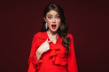 Şok olmuş kırmızı elbiseli bir kadın kendini işaret ediyor. Burgonya arka planında soyutlanmış.