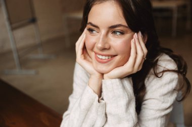 Kafedeki masada otururken uzun kahverengi saçlı, gülümseyen güzel beyaz kadın.