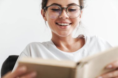 Gözlüklü neşeli beyaz kadının oturma odasındaki kanepede otururken kitap okuduğu bir resim.