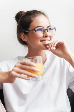 Gözlüklü güzel bir kadının oturma odasında kanepede otururken meyve suyu içtiğini hayal et.