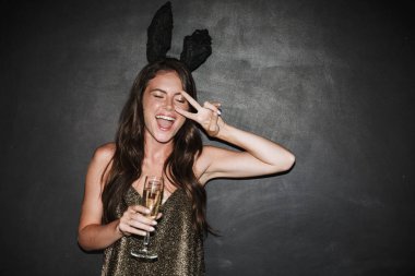 Siyah arka planda izole edilmiş süslü elbiseler giyen güzel genç kız şampanya içiyor.