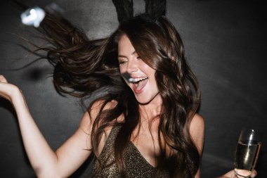 Siyah arka planda izole edilmiş süslü elbiseler giyen güzel genç kız şampanya içiyor.