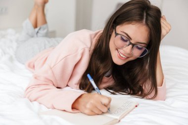 Yatak odasında pijama giyen neşeli, genç bir kız. Bir günlük tutuyor.