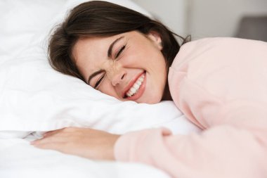 Yatak odasında pijama giyen, yastığa sarılan neşeli, genç bir kız.