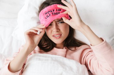 Yatak odasında pijama giymiş, uyku maskesi takmış üzgün genç bir kız.