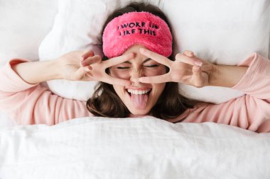 Yatak odasında pijama giymiş, uyku maskesi takmış neşeli bir genç kız.