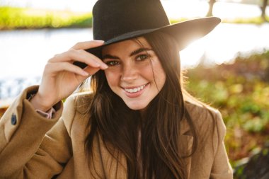 Sonbahar parkında bankta otururken gülümseyen esmer bir kadının portresi.