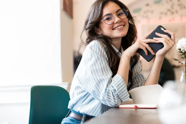 Adorável Sorrindo Jovem Morena Sentada Mesa Café Dentro Casa Usando — Fotografia de Stock