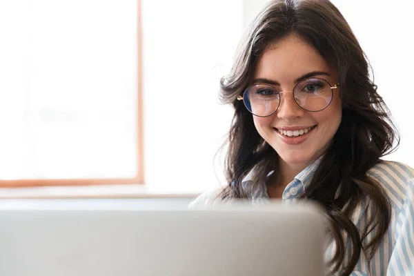 素敵な笑顔若いブルネットの女性がカフェテーブルに座って屋内で ラップトップコンピュータで作業 — ストック写真