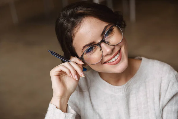 若い美人の白人女性が眼鏡をかけて笑顔でペンを持っている姿をカフェでイメージ — ストック写真