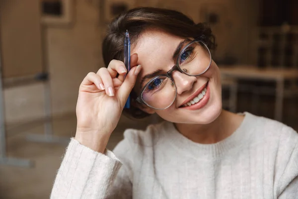 若い美人の白人女性が眼鏡をかけて笑顔でペンを持っている姿をカフェでイメージ — ストック写真