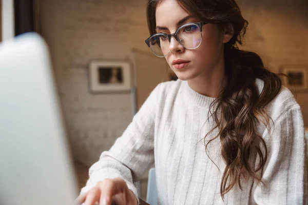 在咖啡店里 年轻美丽的高加索女人戴着眼镜 使用银色笔记本电脑的图片 — 图库照片
