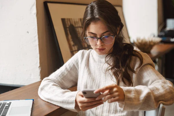 在咖啡店里 年轻美丽的高加索女人戴着眼镜 使用笔记本电脑和智能手机的图片 — 图库照片