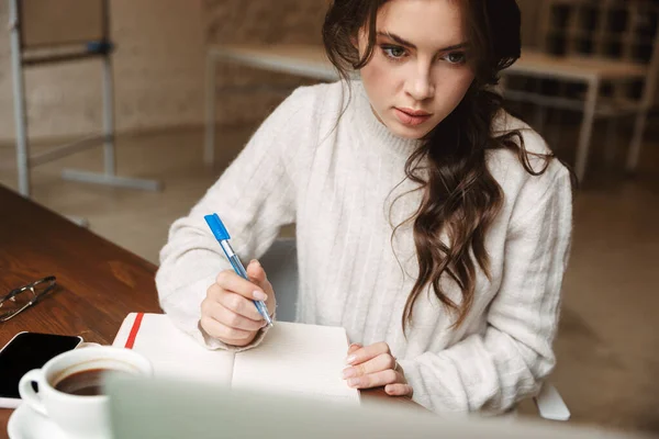 カフェで勉強しながらノートパソコンを使って長い茶色の髪の若い美しい白人女性のイメージ — ストック写真